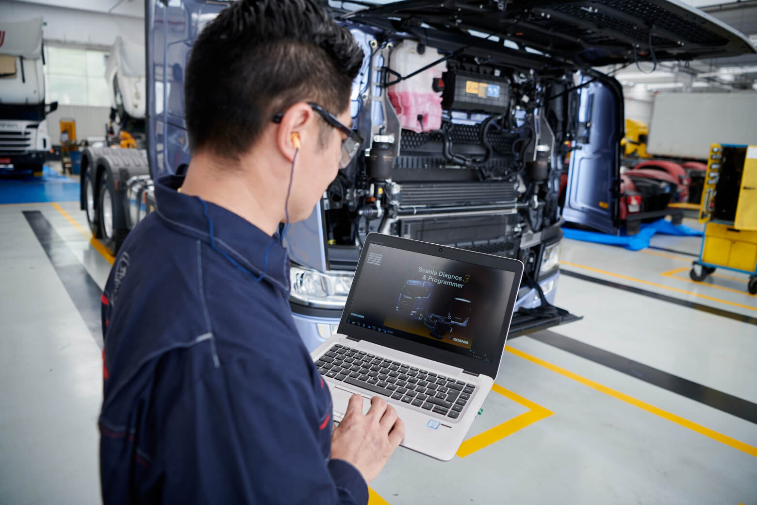 Mechanic wearing earplugs holding a laptop with one hand inside a service center.