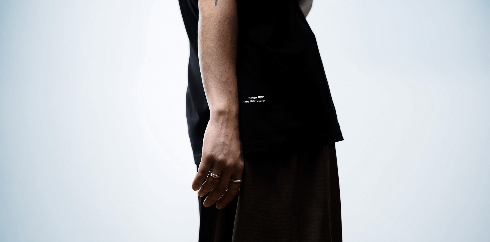 Cropped view of a man's waist, showing the phrase "since 1891, into the future" in small type of a black T-shirt.
