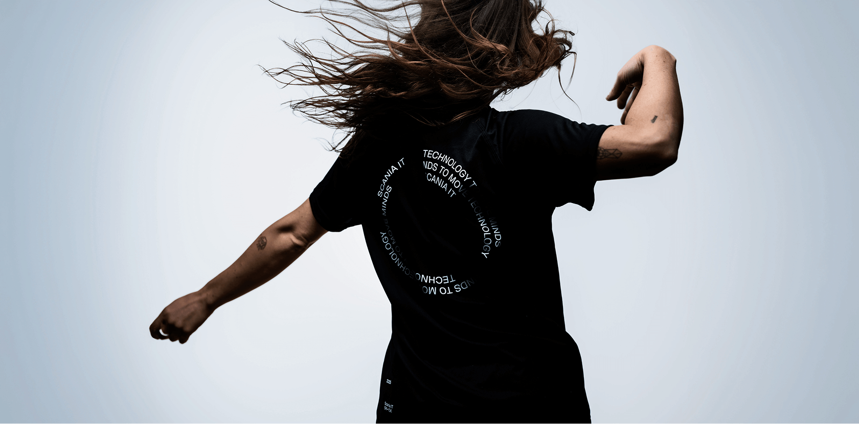 Woman with flowing hair, dancing with her back turned, wearing a black Scania T-shirt.