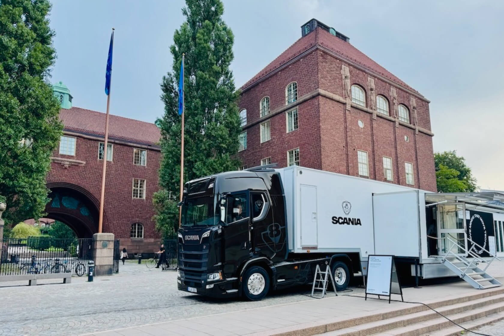 A black Scania truck parked in front of a brick building.
