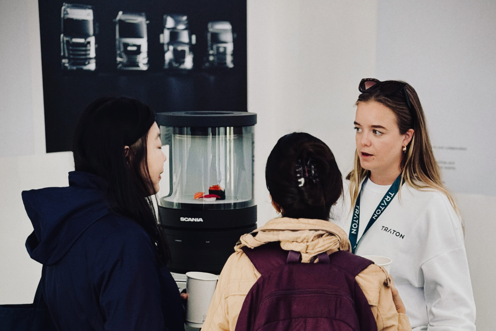 Three women deep in conversation standing in front of a Scania device.