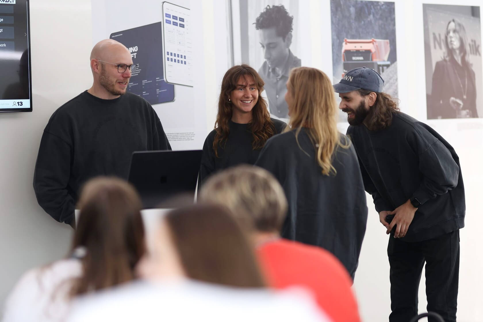 Group of Scania employees smiling and standing in front of Scania posters hanging on a wall.